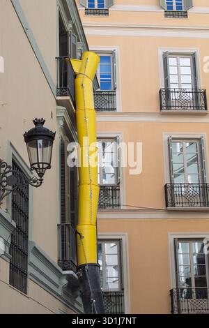 Yellow debris chute extending from a building balcony during urban renovation, managing construction waste in a city environment Stock Photo