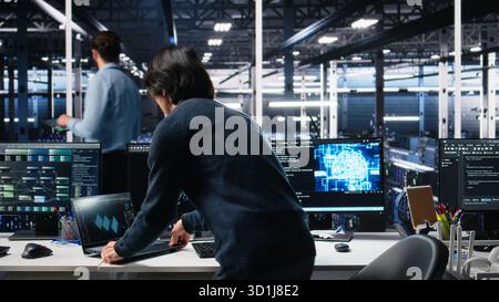 Technician arriving in data center office, coding with generative AI assistance. IT expert sitting at desk, starting work on artificial intelligence large language model solving tasks, camera A Stock Photo
