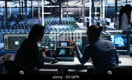 Senior programmer and coworker in data center coding with generative AI assistance. Teamworking colleagues leveraging artificial intelligence large language model to solve tasks, camera A Stock Photo