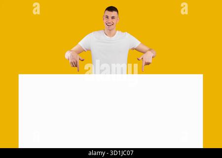 Male Model in a White T-Shirt Gestures Enthusiastically With a Big Smile Against a Bright Yellow Background Stock Photo