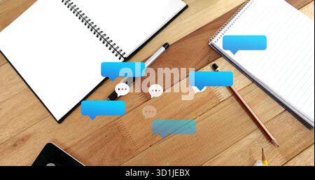 Displaying digital speech bubble icons floating above desk, with notebooks writing tools and tablet Stock Photo