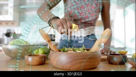 Home cook squeezing lemon juice over green salad at kitchen countertop, with wooden bowl Stock Photo