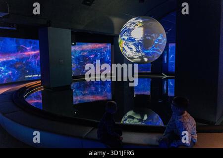 Interactive space museum exhibition with floating Earth globe and cosmic displays showing galaxy nebula on multiple screens in modern planetarium inte Stock Photo