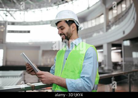 Construction Worker Using Tablet Inside Modern Building Under Construction With Safety Gear Stock Photo