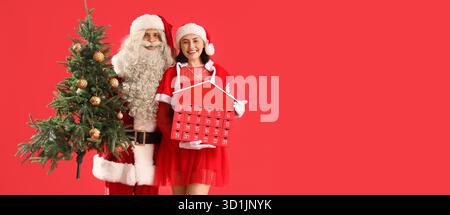Young couple in Santa costumes, with Christmas tree and advent calendar on red background with space for text Stock Photo