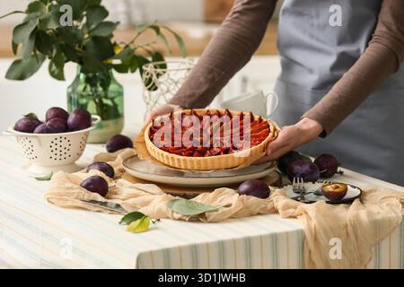 Woman holding tasty plum pie at table in kitchen Stock Photo