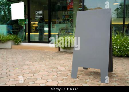 Empty black A-frame sandwich board placed on pavement in front of modern cafe, ideal for restaurant, or business advertising, branding design, product Stock Photo