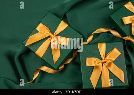 Three green gift boxes with golden ribbons on green silk background. Luxurious gift boxes as a beautiful display. Copy space for the text. Stock Photo