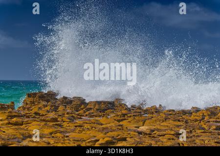 White wave breaking on rock platforms spraying white foam on sunny day with blue sky at North Avoca beach, New South Wales, Australia Stock Photo