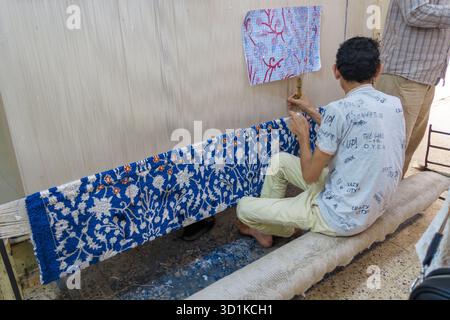 Man sitting on the floor weaving a detailed and colorful rug by hand on a traditional loom in Egypt Stock Photo
