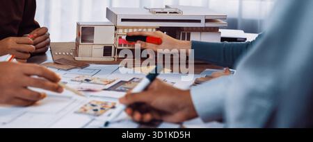 A group of architects collaborates in a modern workspace, examining sketches and a model. Colorful markers and design papers showcase the creative Stock Photo