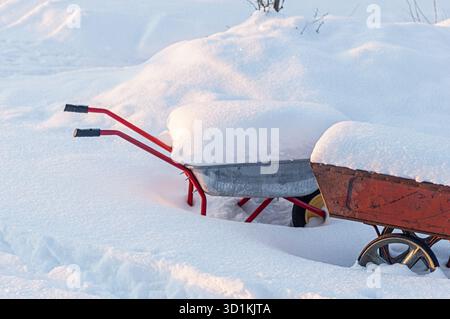 Two garden wheelbarrows covered with fresh white snow stand in a deserted winter landscape. Scene shows garden tools, cold season, outdoor work, rural Stock Photo