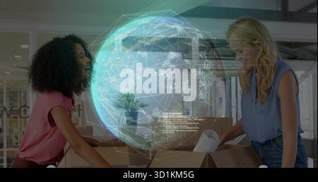 Unpacking two women in office wear reviewing holographic globe at office desk, with cardboard boxes Stock Photo