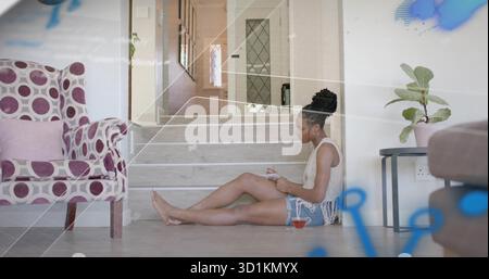Writing Black woman on corridor floor filling notebook with pen, glass tea cup, patterned chair Stock Photo