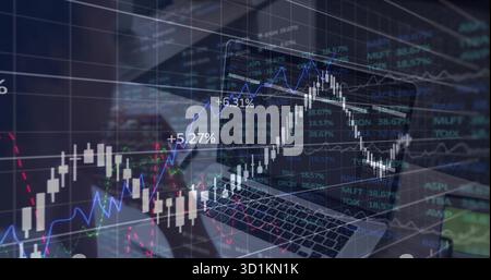 Displaying laptop showing trading charts with percentages on office desk, with smartphone nearby Stock Photo