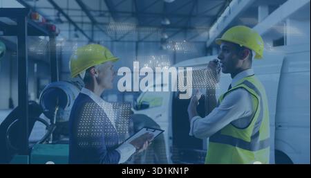 Project manager and site tech in helmets coordinating logistics in warehouse with clipboard, radio Stock Photo