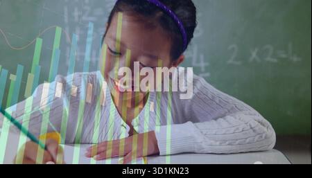 Writing Chinese student solving math problems at desk in class, with chalkboard charts and pencil Stock Photo