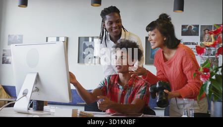 Pointing photographer in orange sweater discussing project on desktop in studio, with DSLR camera Stock Photo