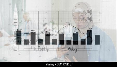 Reviewing nurse in scrubs and stethoscope holding tablet at nurse station, with monitors Stock Photo