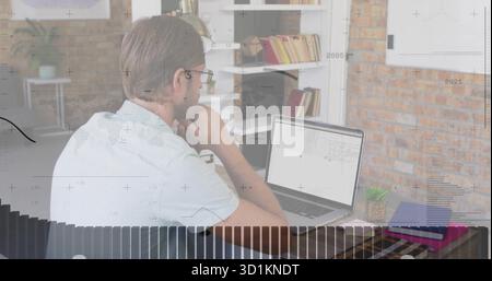 Mid-adult man in blue polo analyzing data on laptop at home office, with bookshelf and succulent Stock Photo
