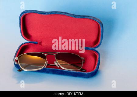 Stylish eyewear resting inside red lined velvet case with blue exterior, photographed on soft gradient blue backdrop highlighting elegant detail Stock Photo