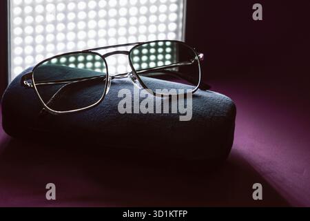 Elegant tinted eyewear placed on textured velvet case, captured with dramatic light and shadow against deep magenta surface for vintage product photog Stock Photo