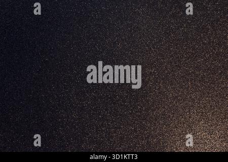 Dark granular glitter background enriched with golden sparkles, warm diagonal light from bottom right forms elegant gradient blending into shadow Stock Photo