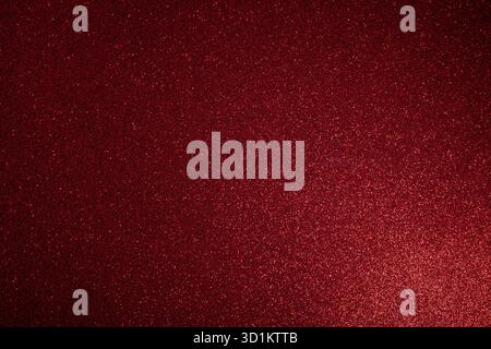 Deep red glitter surface glowing with soft light from lower right, macro focus highlights fine sparkles scattered evenly across textured abstract fram Stock Photo