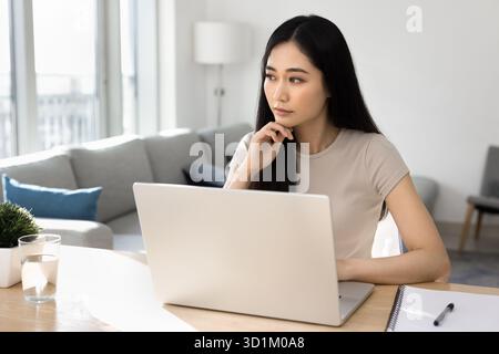 Thoughtful woman working on laptop at home Stock Photo