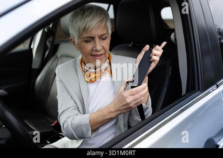 Senior woman sits in car and secures her seatbelt while preparing to drive, showing safety awareness and readiness for the journey ahead. Stock Photo