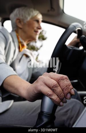 Blurred image of older businesswoman driving a car, focus on a hand holding onto gearshift Stock Photo