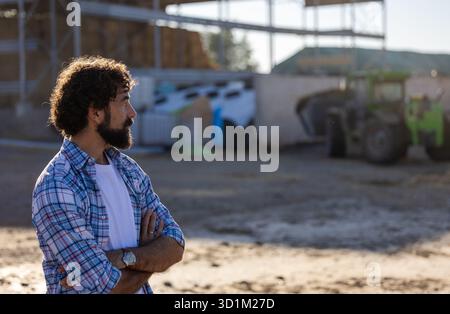 Side profile of curly haired. man on a farm, looking into distance with green tractor in background Stock Photo