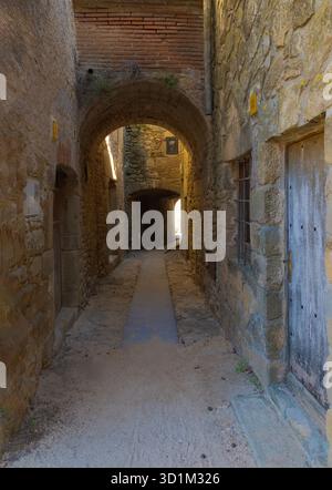 Narrow medieval alleyway in Madremanya's old town with arched stone passages, rustic walls, wooden doors, and soft ambient light. Stock Photo