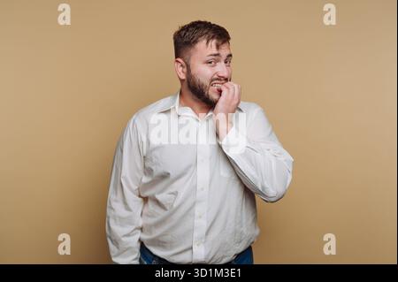 Man in white shirt biting nails, looking anxious. Stock Photo