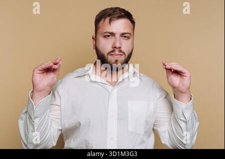 Man in white shirt gesturing with hands against beige background. Stock Photo