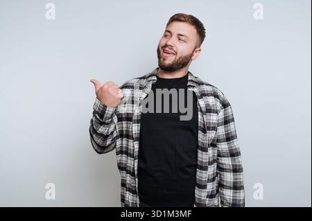 A bearded man in a plaid shirt pointing to the side with a smile. Stock Photo