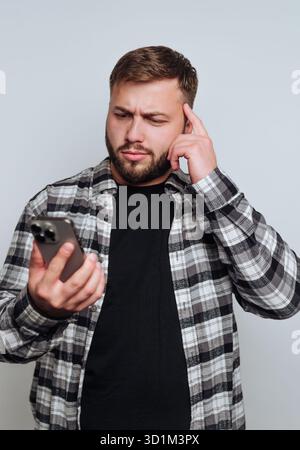 Man in plaid shirt looking confused at smartphone. Stock Photo