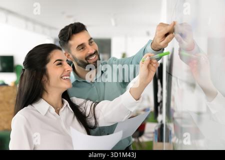 Two happy planners review project timeline on glass marker board Stock Photo