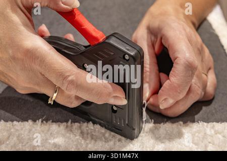 Close up of a black upholstery stapler and metal staples placed on a wooden frame covered with soft white fabric. Concept of furniture renovation, DIY Stock Photo