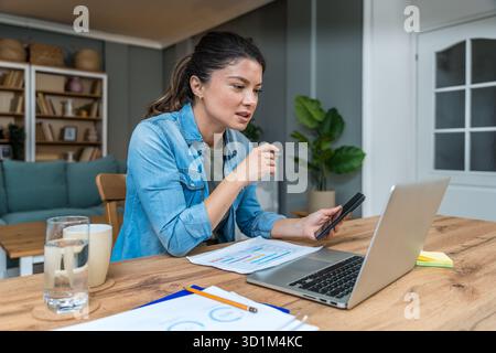 Freelance businesswoman in home office reviewing charts and dictating a voice note while analyzing financial reports on a laptop — remote work, strate Stock Photo