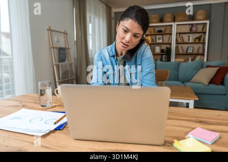 Freelance businesswoman in home office reviewing charts and dictating a voice note while analyzing financial reports on a laptop — remote work, strate Stock Photo