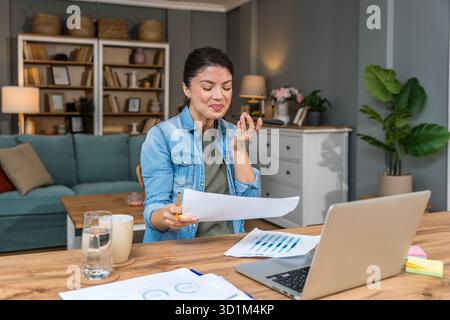 Freelance businesswoman in home office reviewing charts and dictating a voice note while analyzing financial reports on a laptop — remote work, strate Stock Photo
