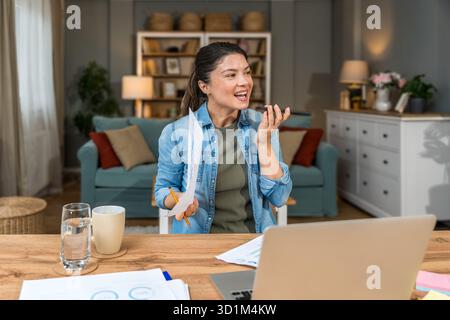 Freelance businesswoman in home office reviewing charts and dictating a voice note while analyzing financial reports on a laptop — remote work, strate Stock Photo