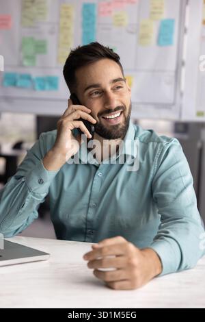Smiling confident male entrepreneur talk on smartphone at office desk Stock Photo