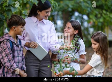 Teacher explaining to pupils importance of taking care of plants, kids having hands-on lesson outdoors Stock Photo