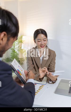 Two business professionals are discussing financial charts and strategies in a modern office. They exchange ideas, analyze reports, and negotiate solu Stock Photo