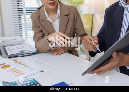 Two business professionals are discussing financial charts and reports in a modern office. They collaborate, share ideas, and analyze data together, h Stock Photo