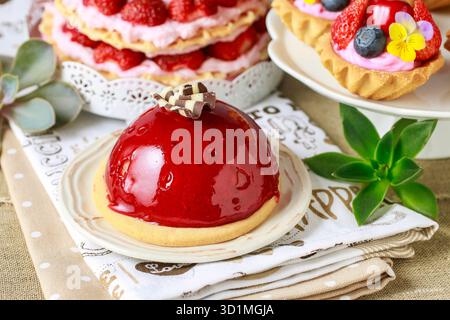 Chocolate cake with red fruit icing. Party table, various cakes in the background. Stock Photo