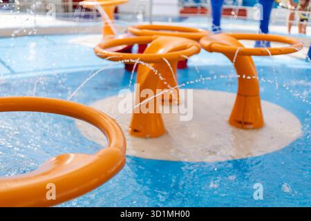 Children enjoy refreshing playtime in a vibrant water park scene with bright orange fountains and splashes, creating a joyful atmosphere on a sunny da Stock Photo