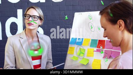 Women wearing blazer, blouse placing sticky notes on flip chart in office, with neon overlay icons Stock Photo